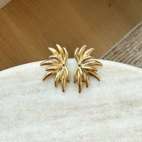 Gold leaf-shaped earrings on a white stone surface with a wooden background