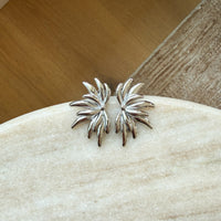 Silver leaf-shaped earrings on a stone surface with a wooden background