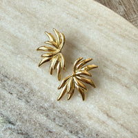 Gold leaf-shaped earrings on a textured stone surface