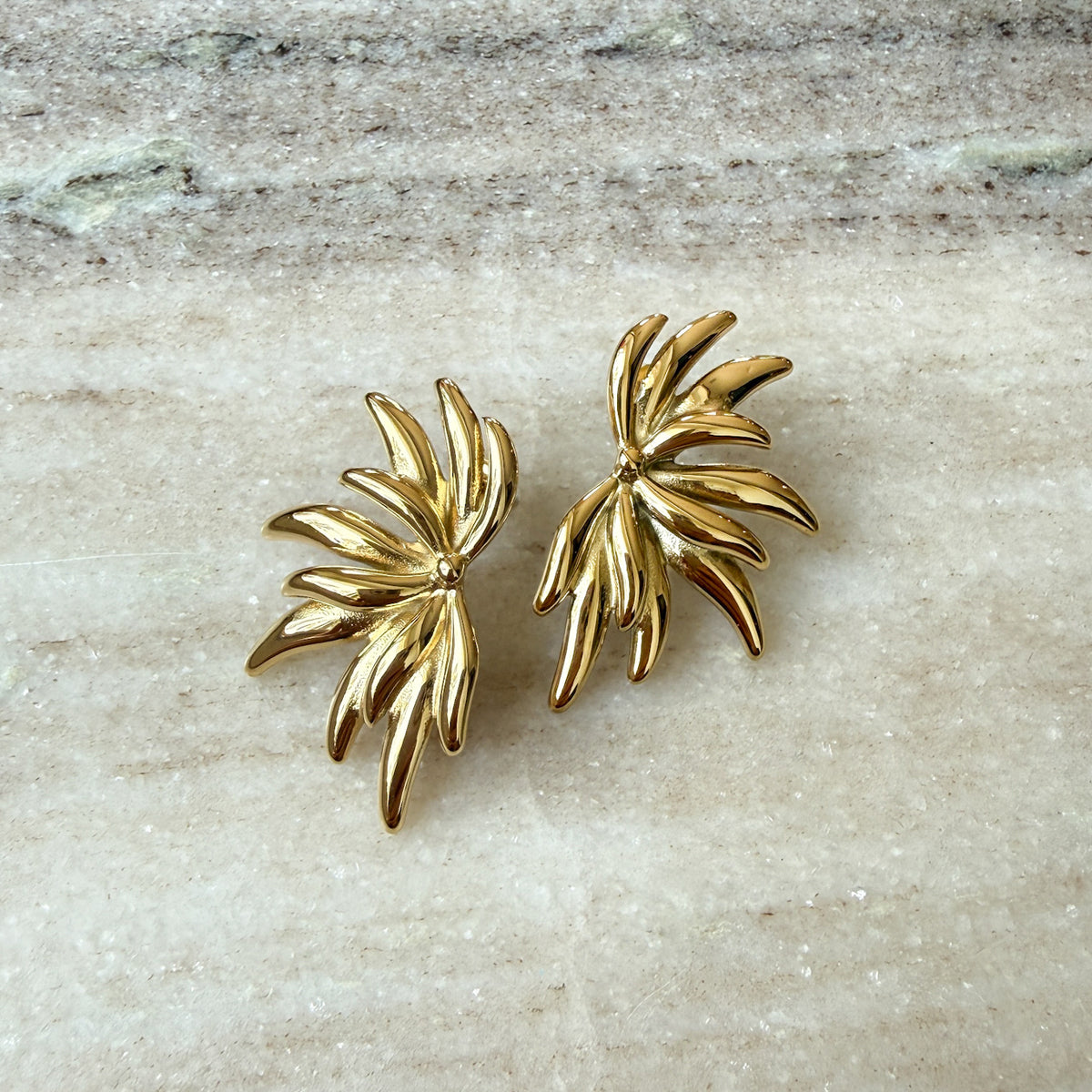 Pair of gold leaf-shaped earrings on a light stone surface -0 Fireworks Statement Earrings - The Songbird Collection