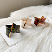 Three tortoiseshell-style cuff bracelets on a white fur surface.