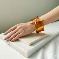 Hand wearing a large amber bracelet on a neutral background. Gaia Sculptural Statement Bracelet - The Songbird Collection