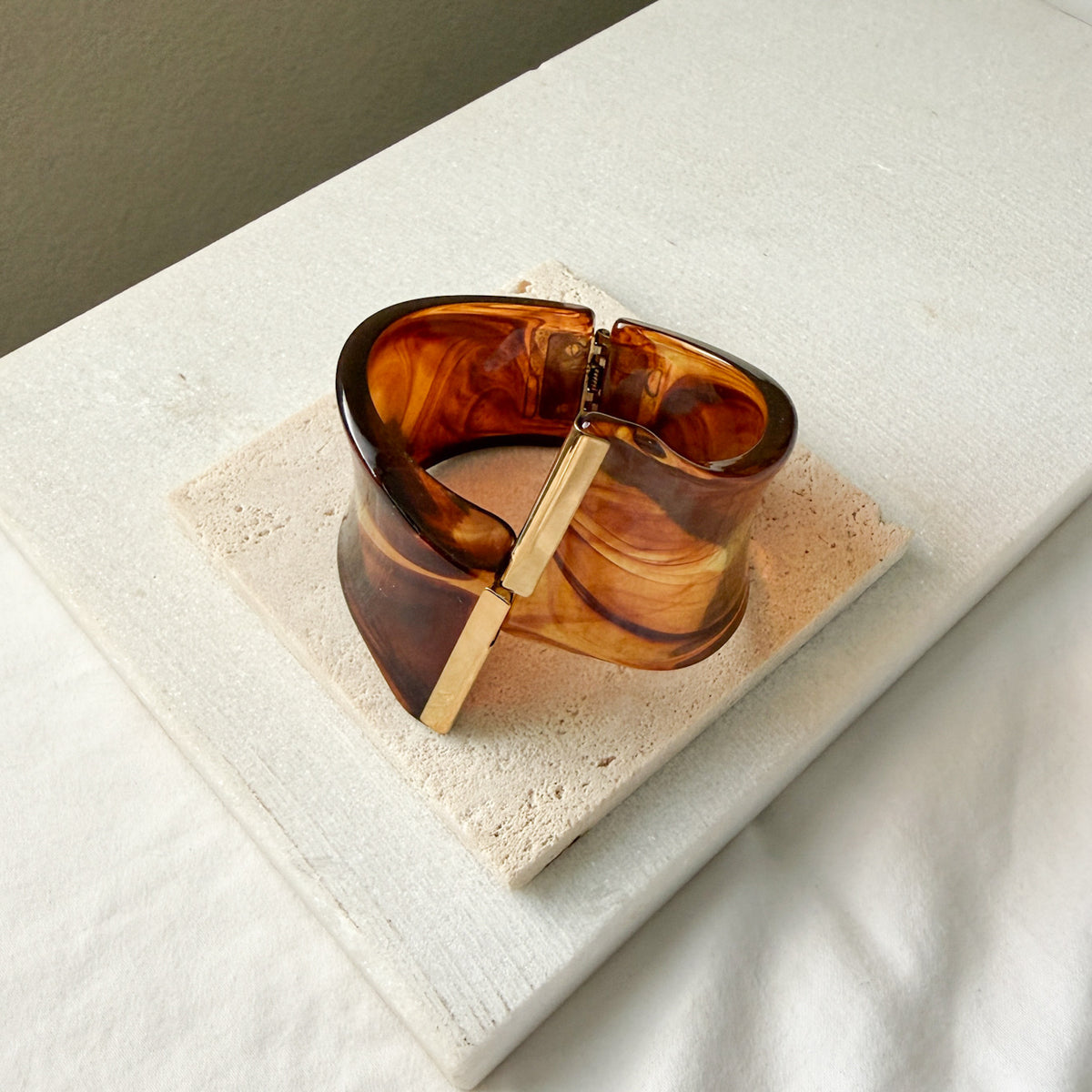 Brown tortoiseshell bracelet with gold clasp on a textured stone surface