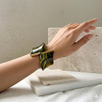 Hand wearing a green and gold bracelet on a neutral background.Gaia Sculptural Statement Bracelet - The Songbird Collection