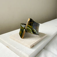 Green and gold bracelet on a white surface with a neutral background