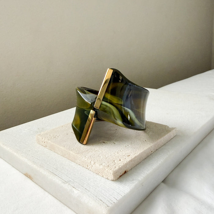Green and gold bracelet on a white surface with a neutral background