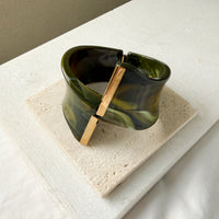 Green marbled cuff bracelet with gold clasp on a beige stone surface