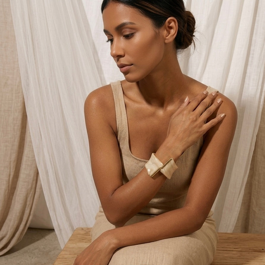 Woman in a beige dress sitting on a wooden bench with white curtains in the background