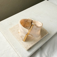 Gold and beige cuff bracelet on a textured surface