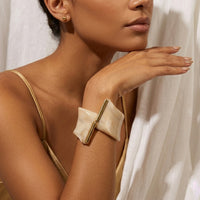 Woman wearing a gold and beige bracelet with a neutral background