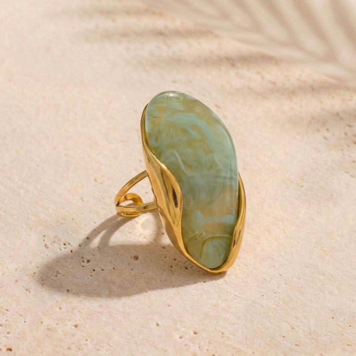 Gold ring with a large green stone on a beige surface