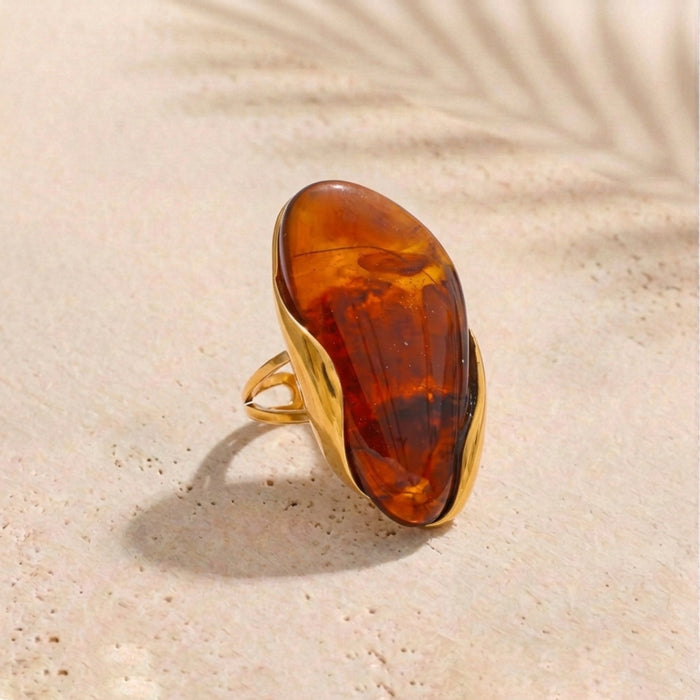 Gold ring with a large amber stone on a beige background
