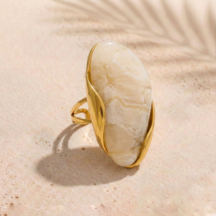 Gold ring with a large beige stone on a sandy background