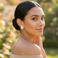 Woman wearing a white flower stud earring with a blurred natural background