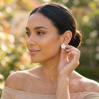 Woman wearing a white floral stud earring outdoors with a blurred natural background
