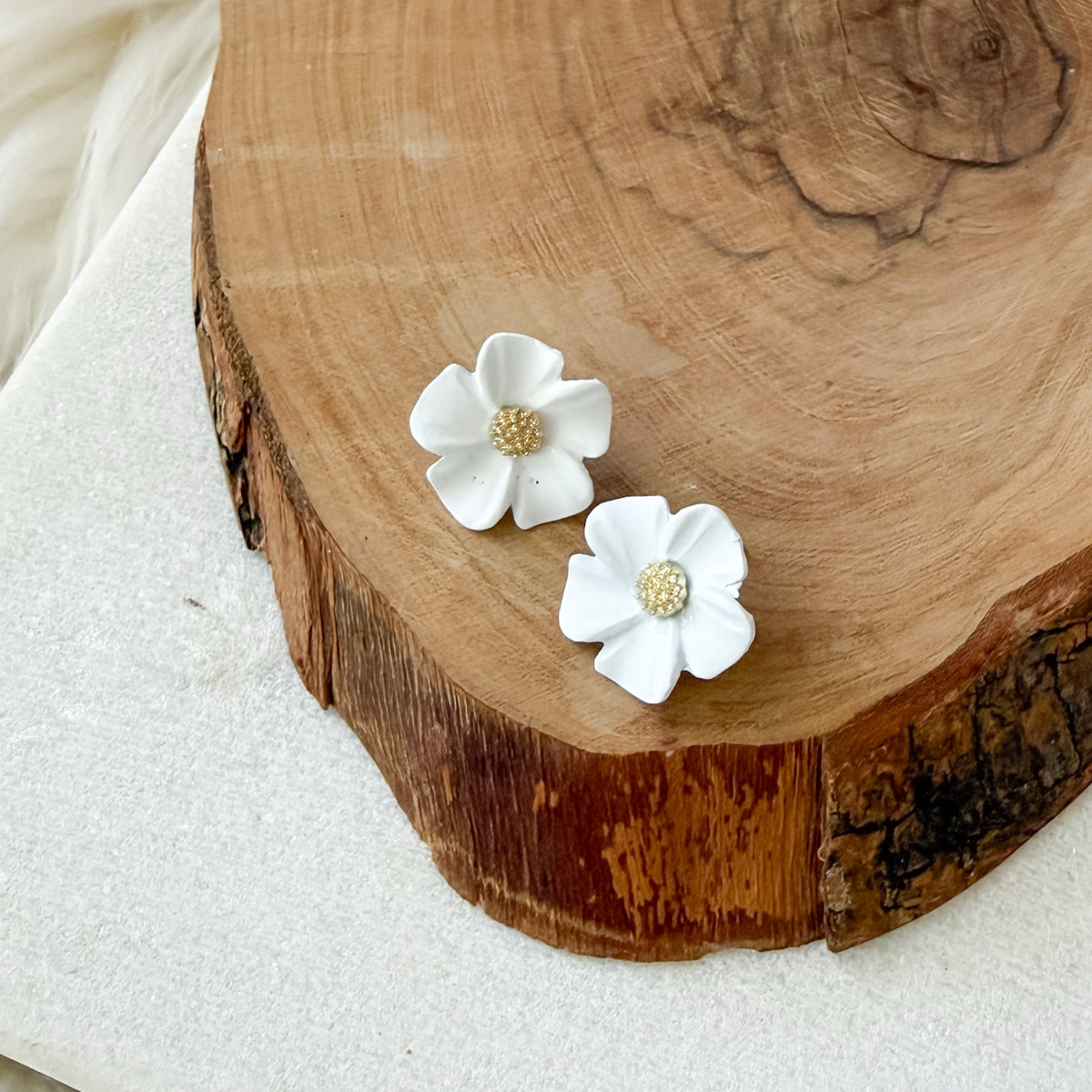 White floral earrings with gold centers on a wooden surface