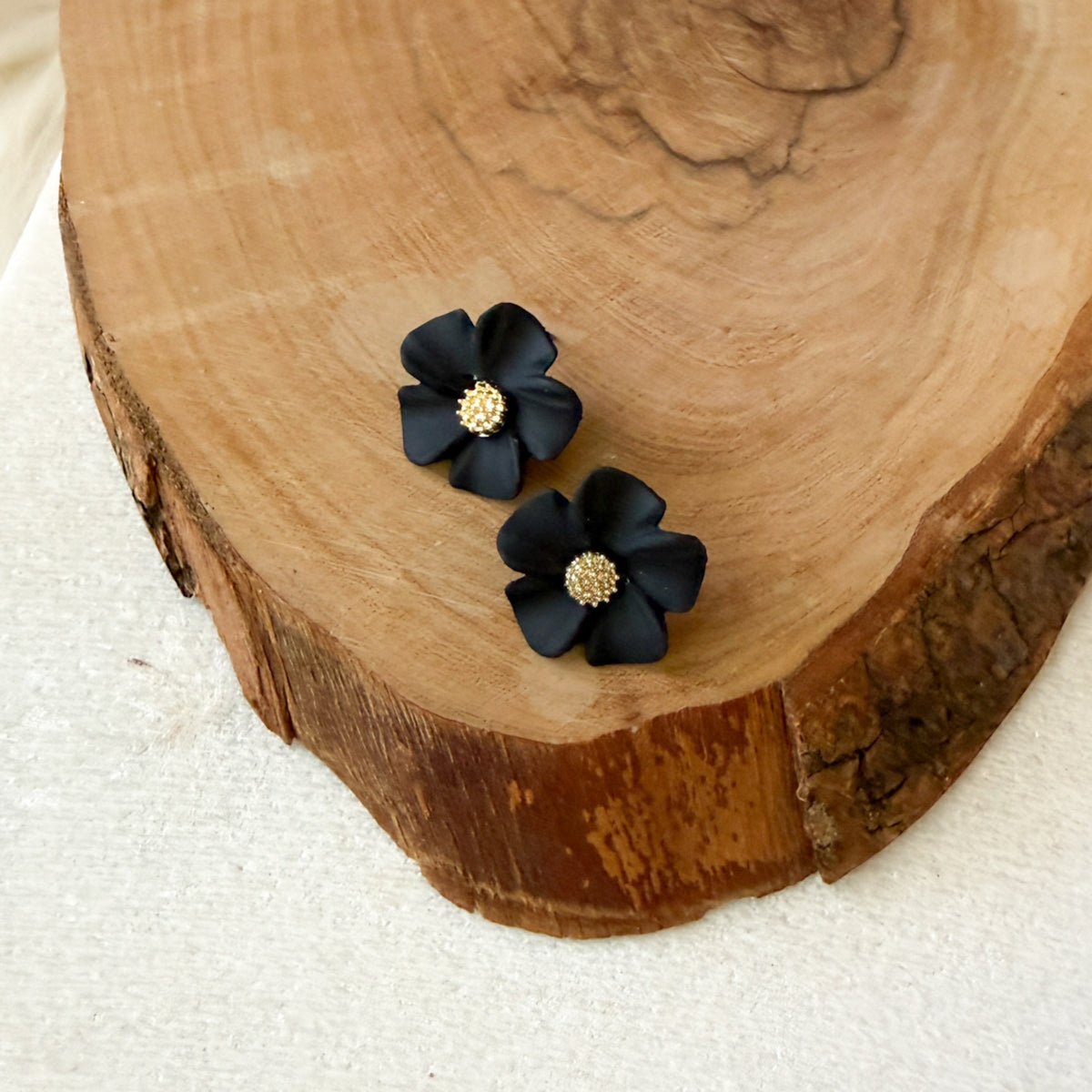 Black flower-shaped earrings with gold centers on a wooden surface