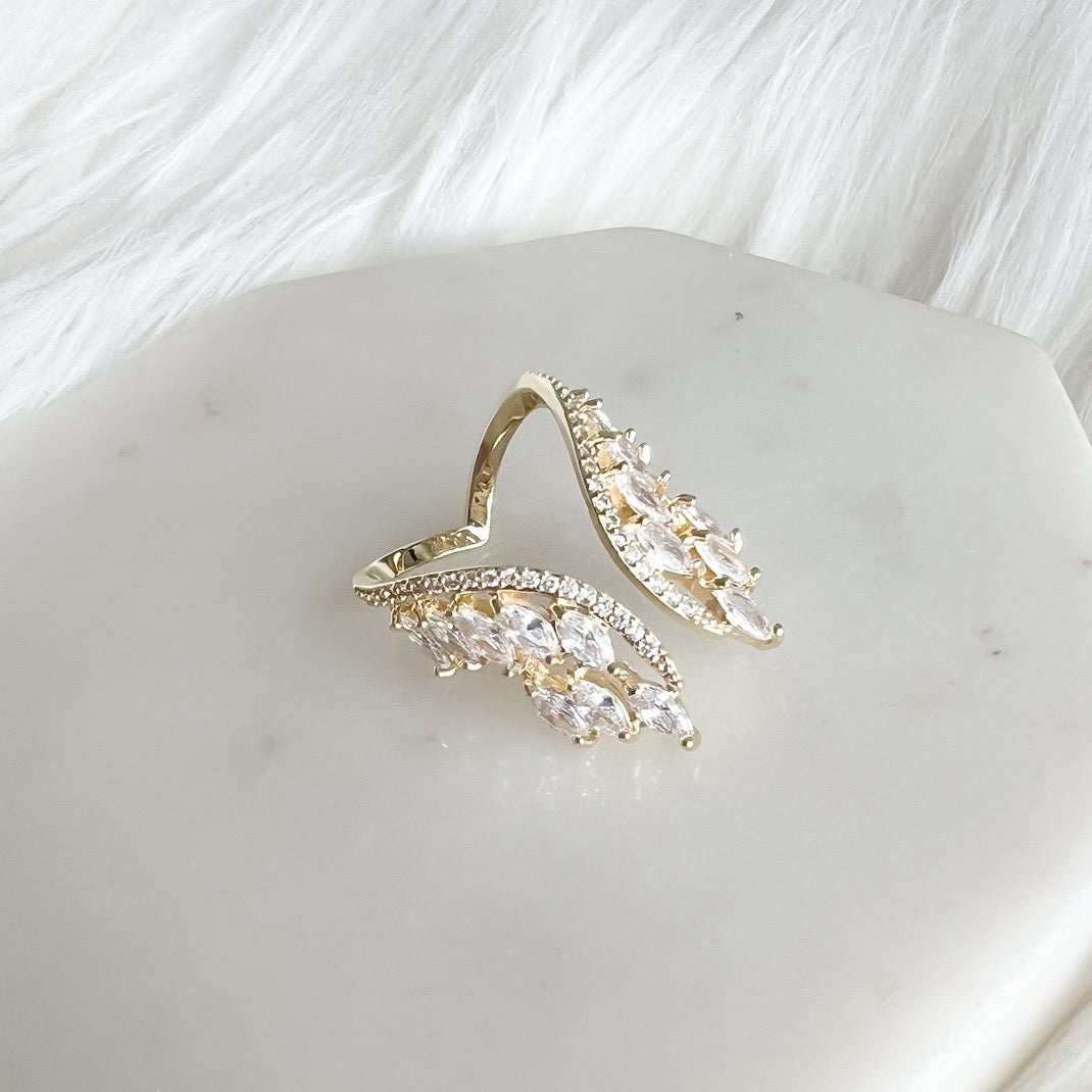 A hand showcasing a silver-colored chandelier ring with cubic zirconia on a finger, with multi-colored nails.