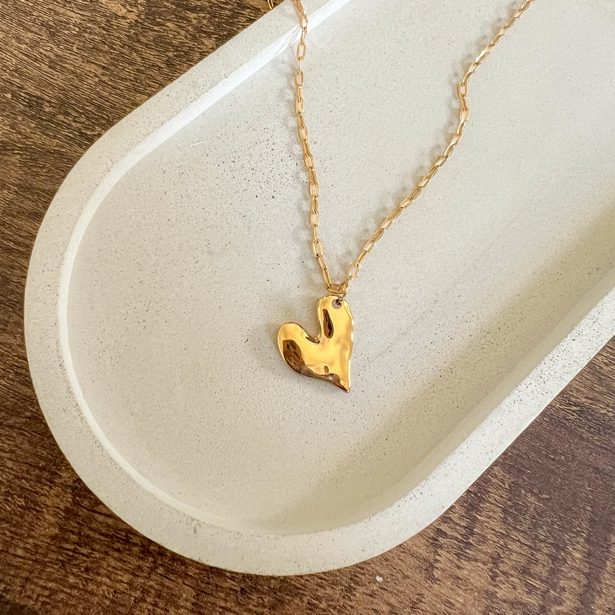 A gold-plated hammered heart pendant necklace on a chain, displayed on a white dish.