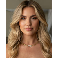 Woman with long blonde hair wearing a gold necklace against a neutral background