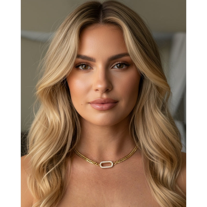 Woman with long blonde hair wearing a gold necklace against a neutral background