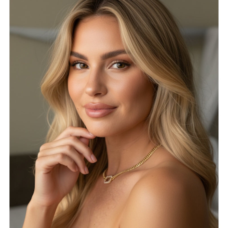 Woman with blonde hair wearing a gold necklace, posing indoors.