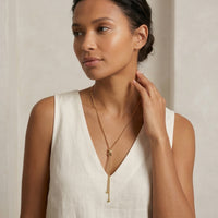 Woman wearing a gold necklace against a neutral background - Infinity Knot Lariat Necklace - The Songbird Collection