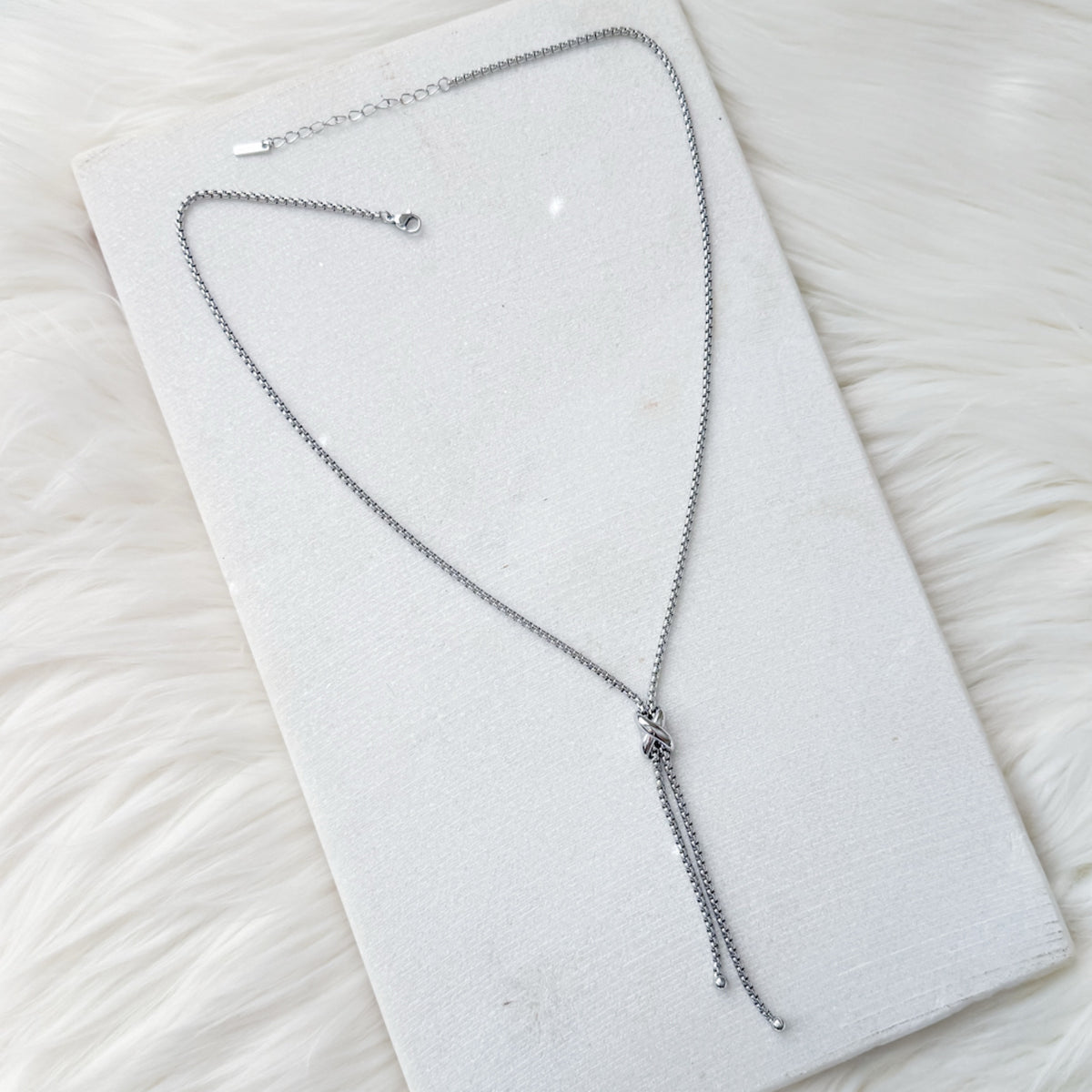 Silver necklace on a white textured surface I- nfinity Knot Lariat Necklace - The Songbird Collection