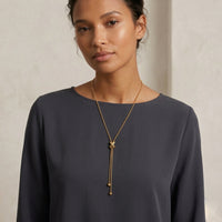 Woman wearing a gold necklace against a neutral background Infinity Knot Lariat Necklace - The Songbird Collection
