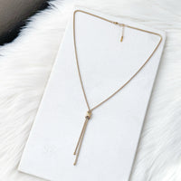 Gold necklace on a white card with a fur background Infinity Knot Lariat Necklace - The Songbird Collection