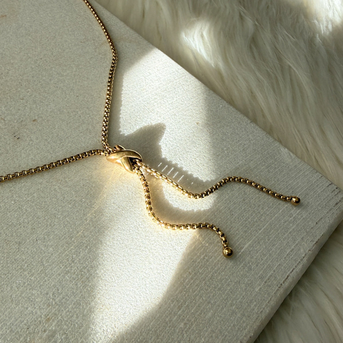 Gold necklace on a textured surface with soft lighting - Infinity Knot Lariat Necklace - The Songbird Collection