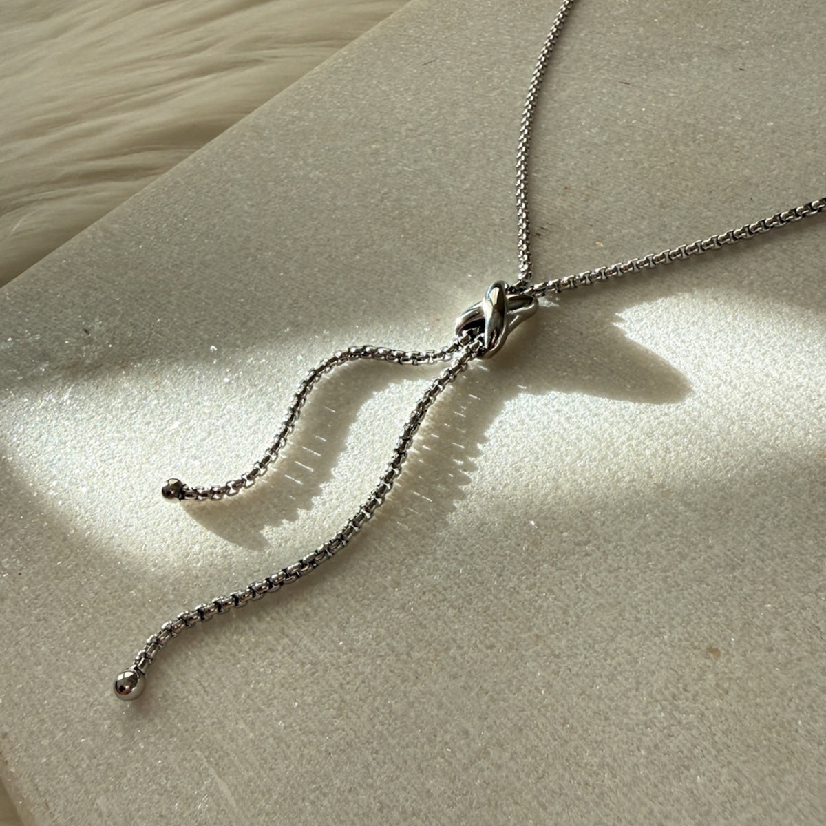 Silver necklace on a textured beige surface - Infinity Knot Lariat Necklace - The Songbird Collection