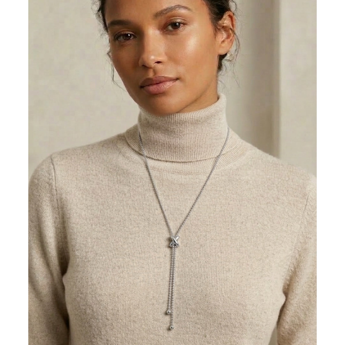 Woman wearing a beige turtleneck sweater with a long necklace against a neutral background - Infinity Knot Lariat Necklace - The Songbird Collection