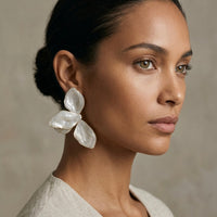 Woman wearing large, white floral earrings against a neutral background  Ivory_Lotus_Statement_Earrings_-_The_Songbird_Collection