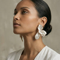 Woman wearing large floral earrings against a neutral background  Ivory_Lotus_Statement_Earrings_-_The_Songbird_Collection
