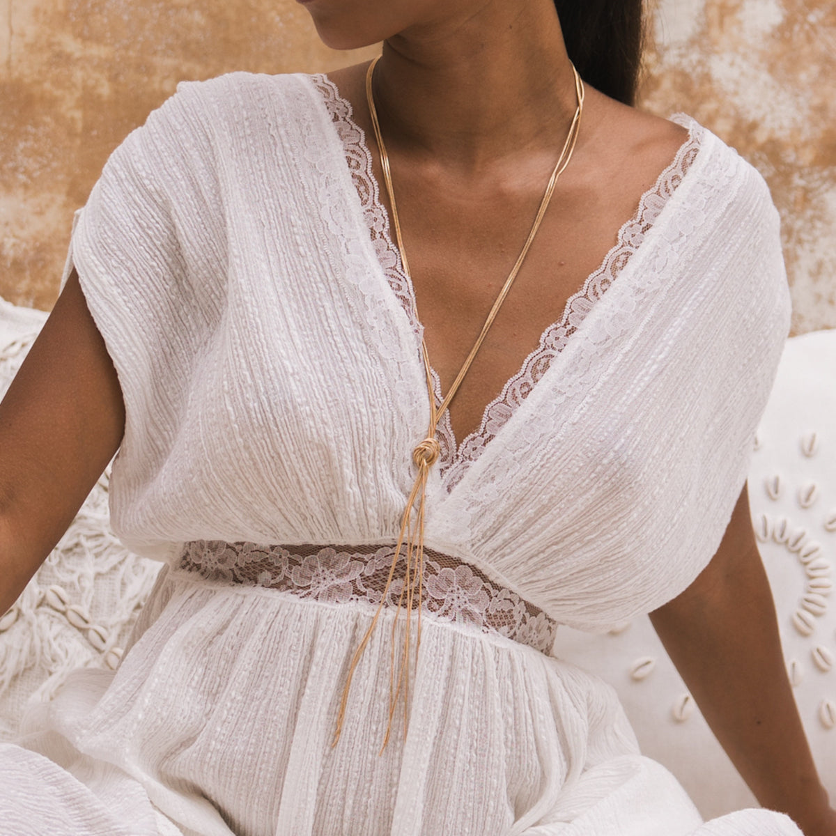 Close-up of a woman wearing a white dress with lace details and a gold necklace.