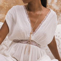 Close-up of a woman wearing a white dress with lace details and a gold necklace.
