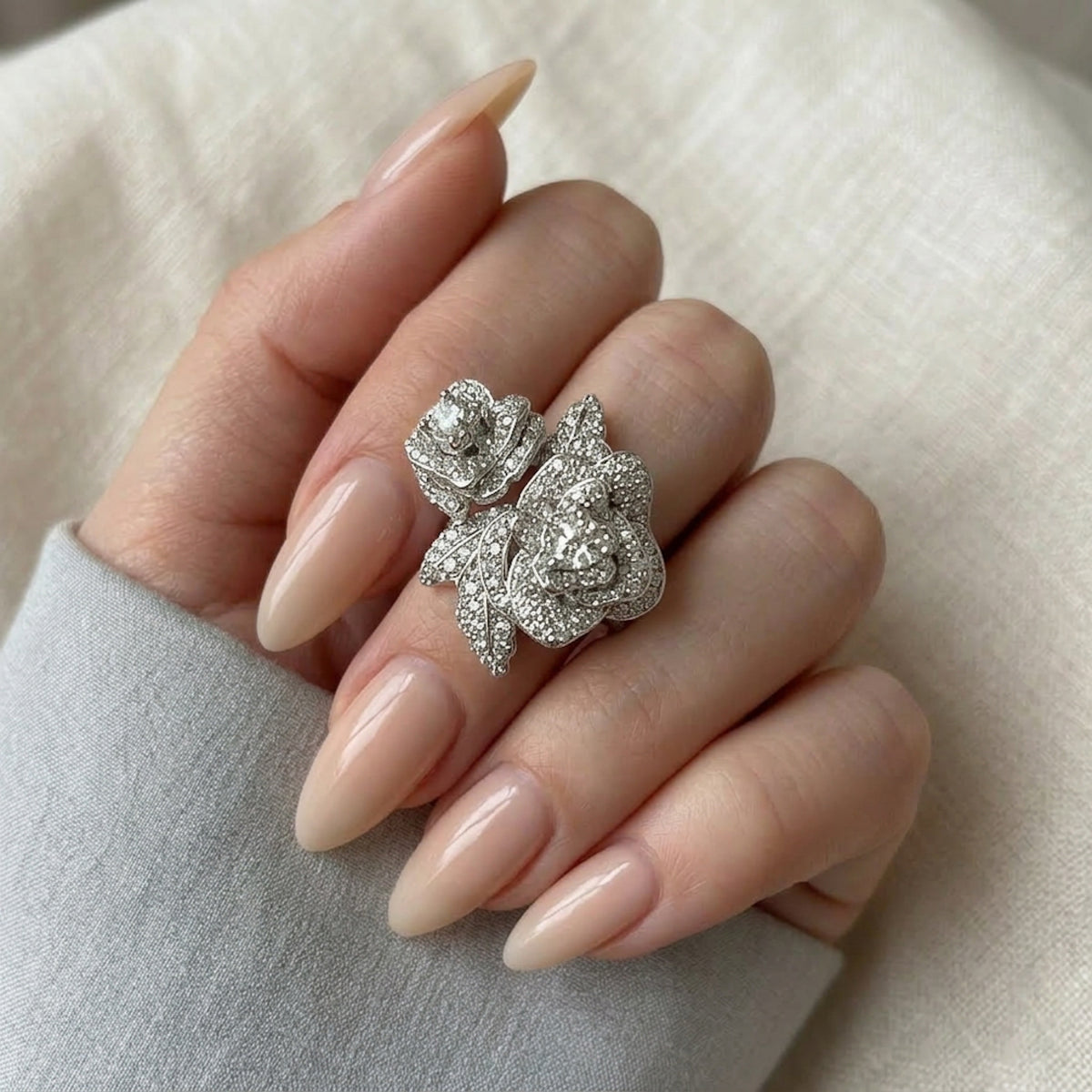 Silver floral ring on a hand with beige nails against a neutral background