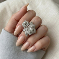 Silver floral ring on a hand with beige nails against a neutral background