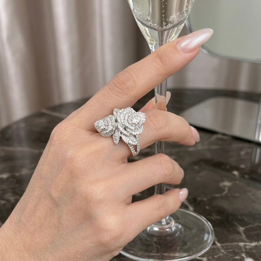 Hand holding a champagne flute with a silver floral ring on a marble surface