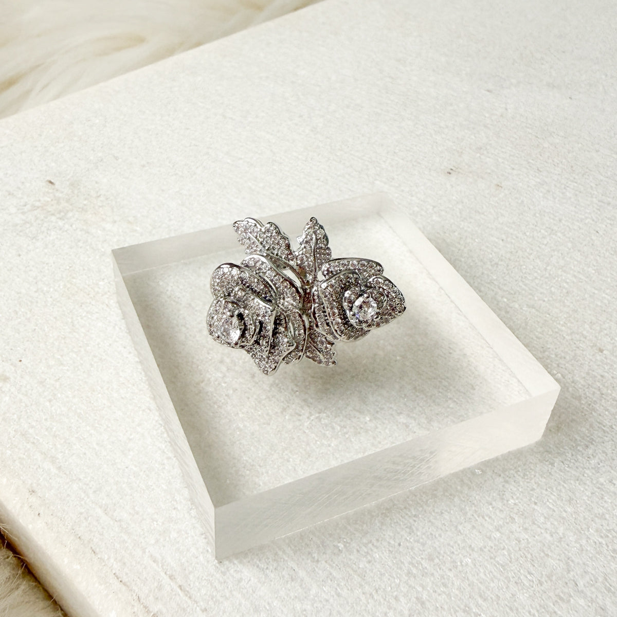 Silver floral ring on a clear acrylic stand with a white background