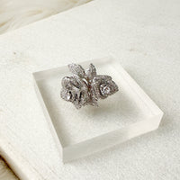 Silver floral ring on a clear acrylic stand with a white background