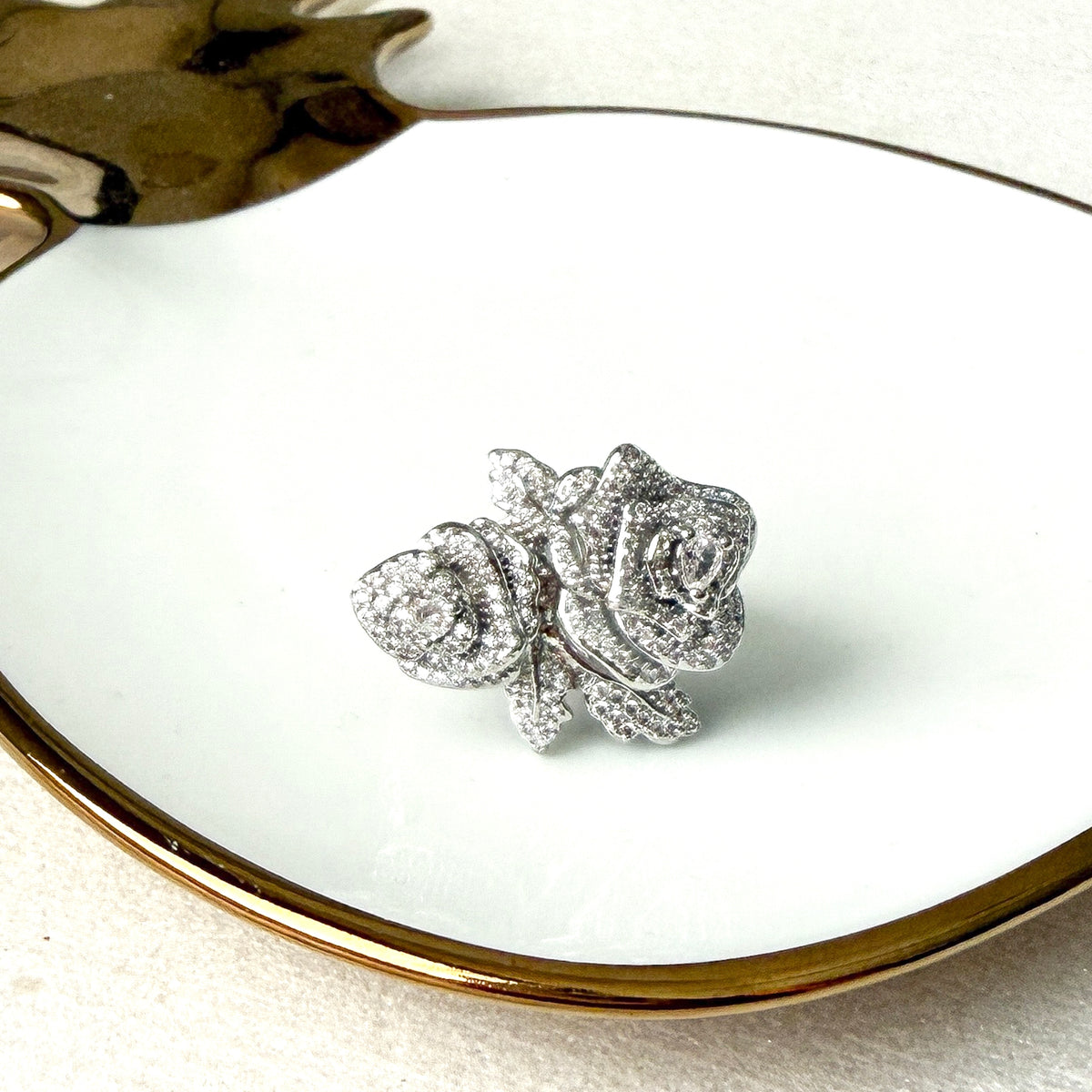 Silver rose-shaped jewelry on a white plate with gold rim