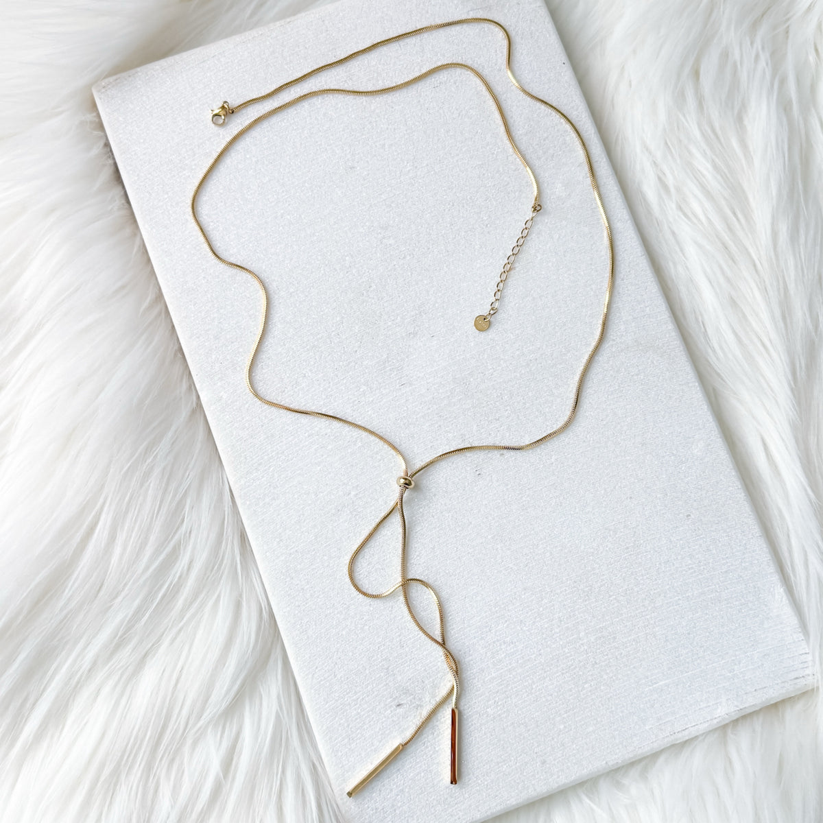 Gold necklace on a white card with a white fur background