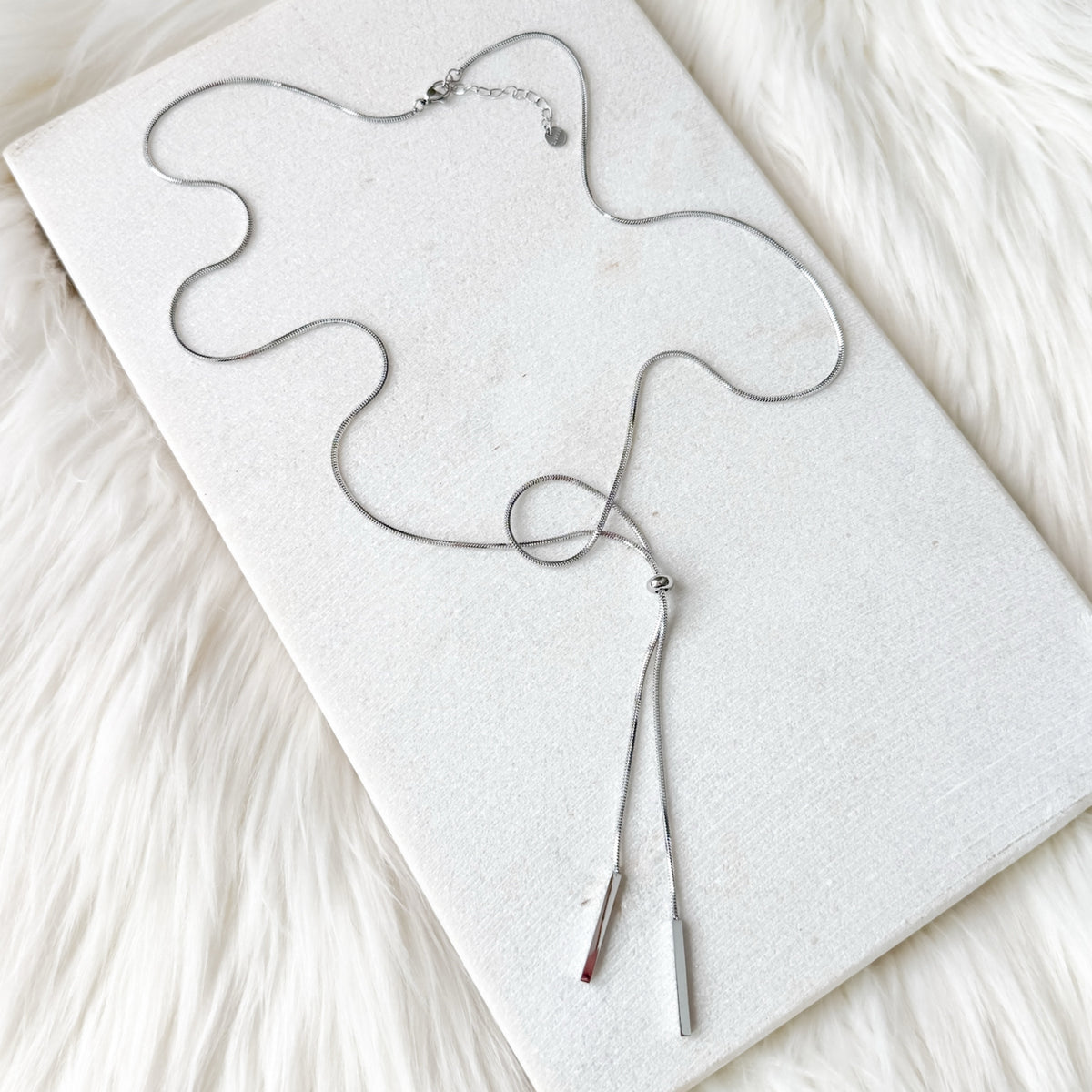 Silver necklace on a white card with a soft white background