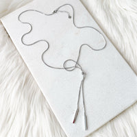 Silver necklace on a white card with a soft white background