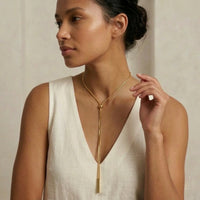 Woman wearing a gold necklace against a neutral background