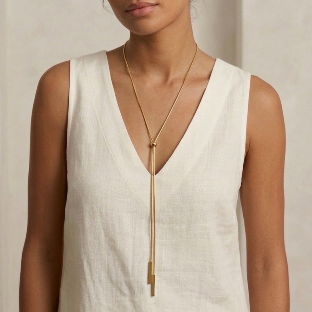 Woman wearing a white sleeveless top and a gold necklace against a neutral background - Linearity Lariat Necklace - The Songbird Collection