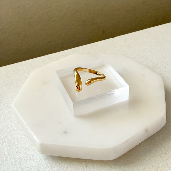 Gold ring on a white marble stand with a beige background  Liquid Curve Ring - The Songbird Collection