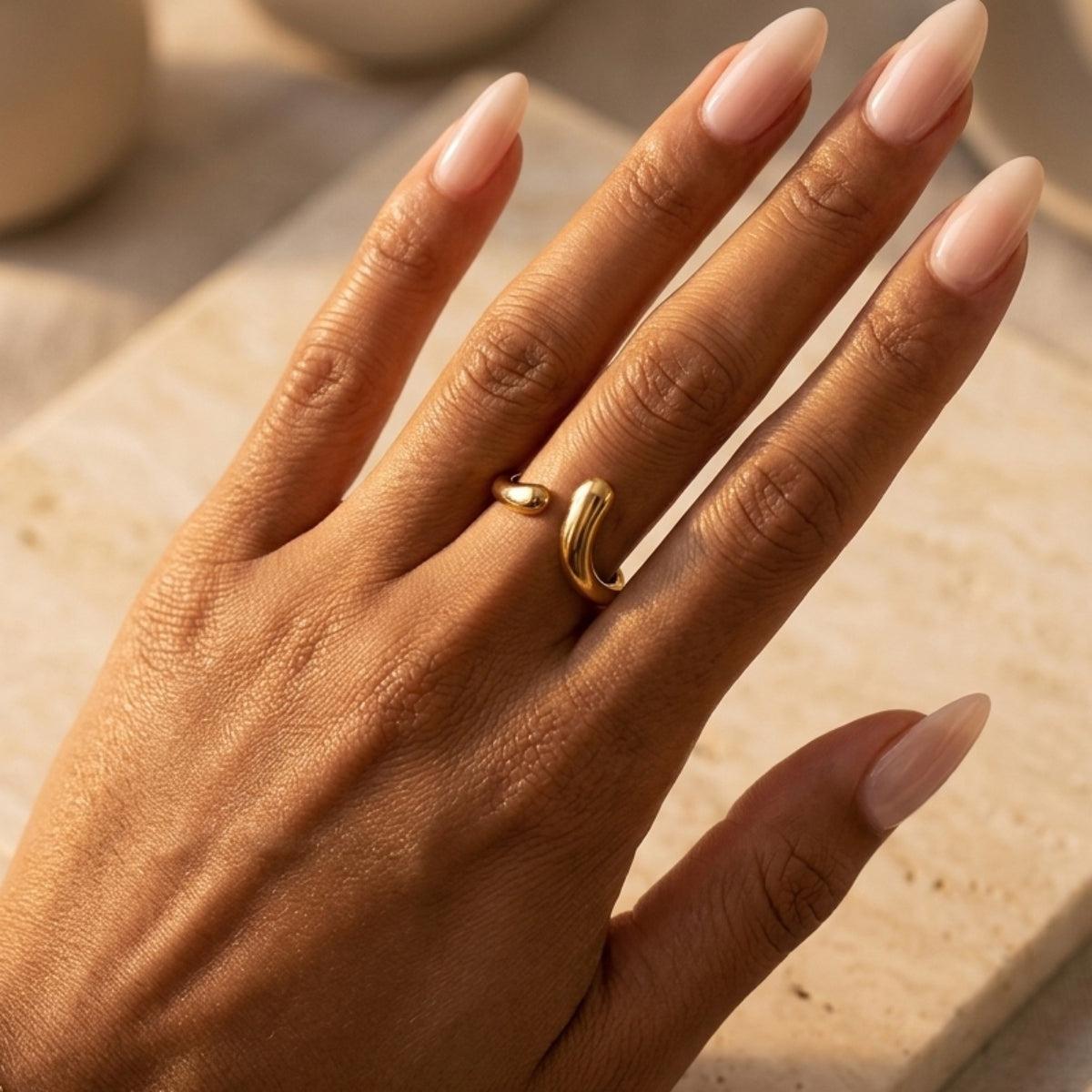 Hand wearing a gold ring with beige nail polish on a neutral background  Liquid Curve Ring - The Songbird Collection
